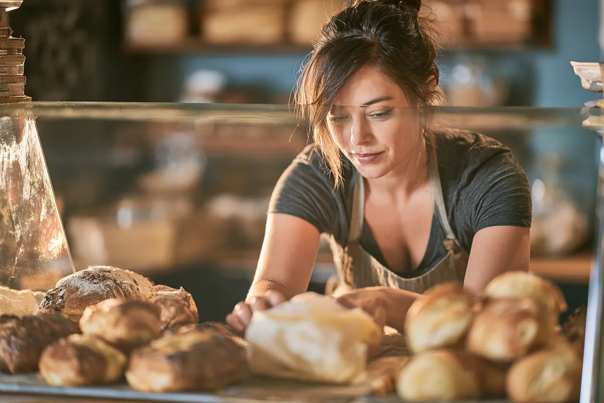 Bakery owner arranging fresh pastries in a glass case at her small shop, a micro business that might use a $5,000 loan