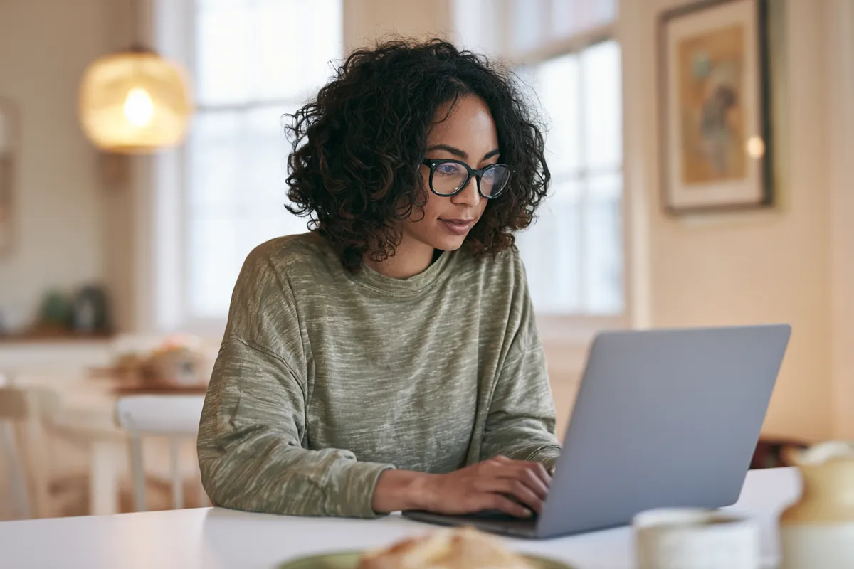 Woman typing on a laptop at a bright dining table while filling out a Willow Lake Loan request
