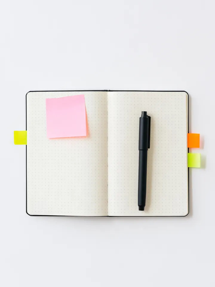 Open dotted notebook with colorful sticky tabs and a black pen, used to note loan questions