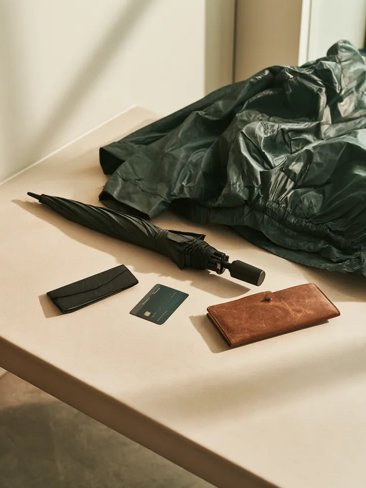 Folding umbrella, transit card and rain jacket on an entryway bench, ready for an unexpected day